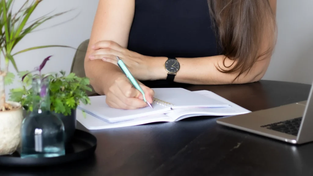 VA Britt schrijft in schrift met laptop en planten op tafel