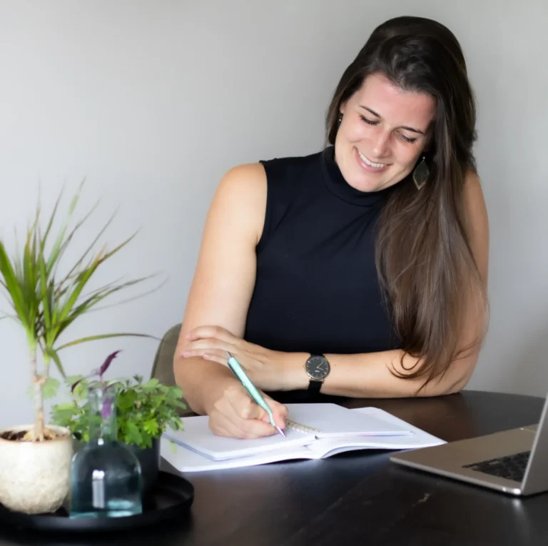 VA Britt lachend schrijvend in schrift met laptop, pen in hand