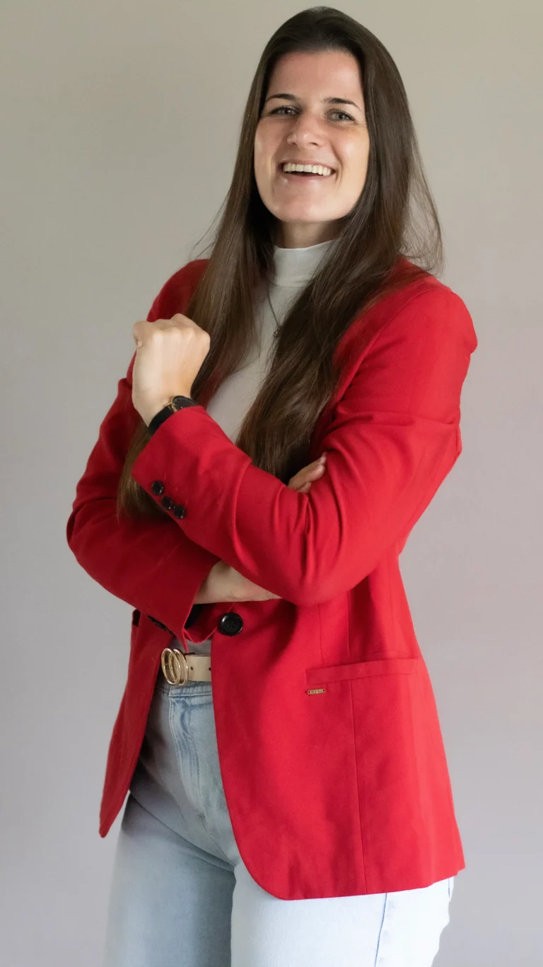 VA Britt lachend met rood colbert en spijkerbroek, handen over elkaar